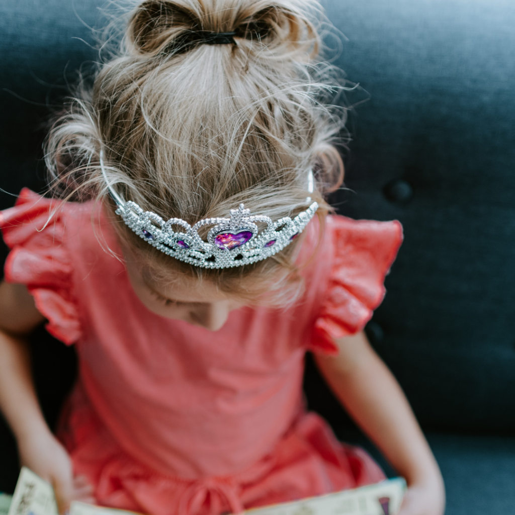 Young girl dressed as a princess reading a fairytale book.